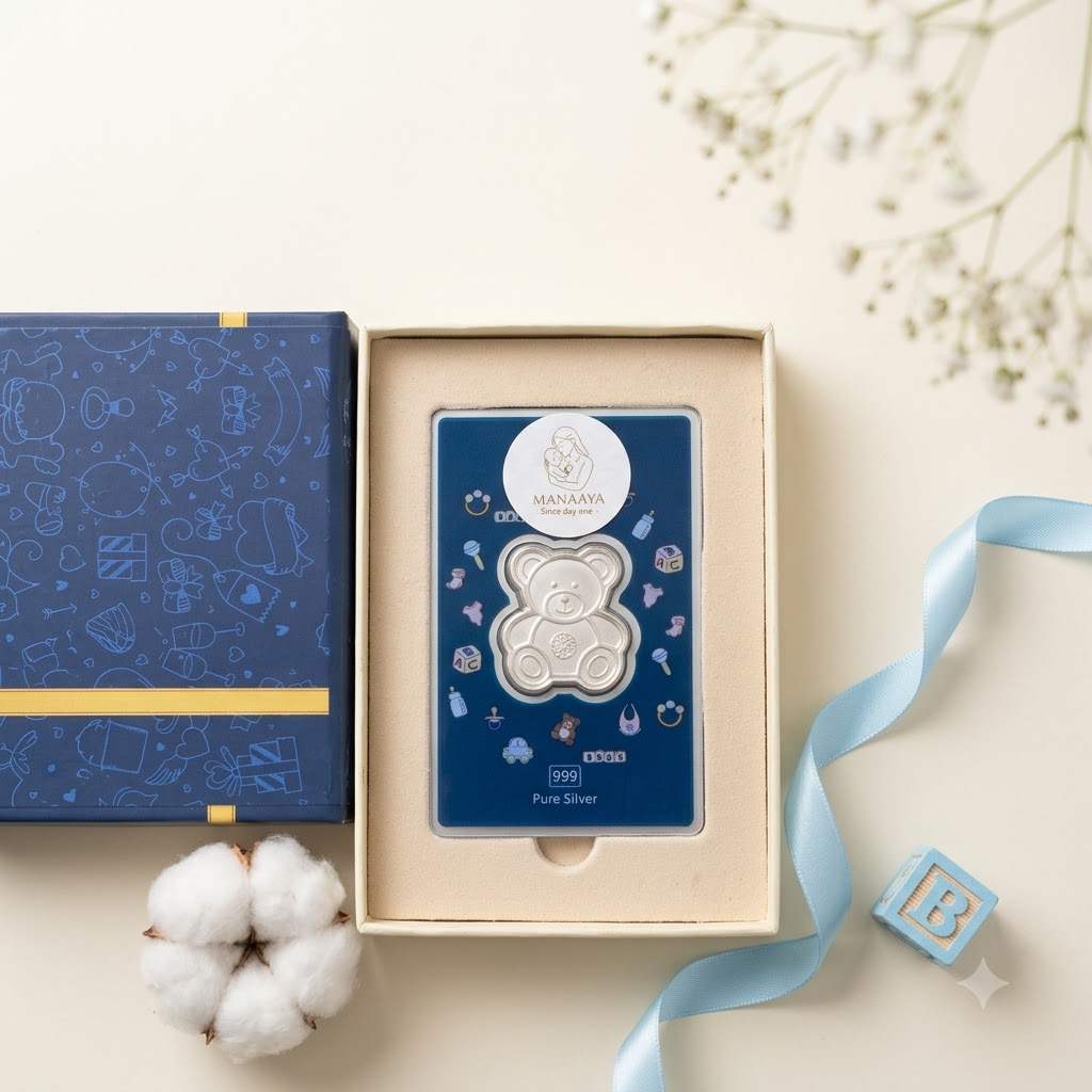 Manaaya teddy bear-shaped silver coin in a cream box beside a navy lid and blue ribbon