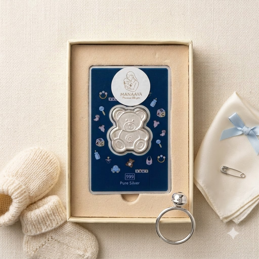 Teddy bear-shaped silver coin on a navy card in a cream box, styled with baby accessories